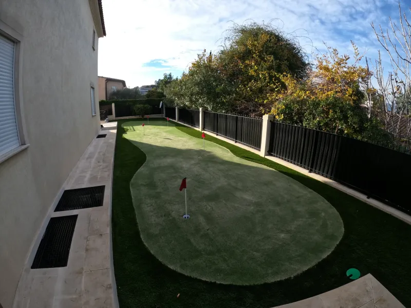 longue perspective sur le putting green, sa forme souple et ses quatre trous intégrés dans un jardin étroit parfaitement structuré.